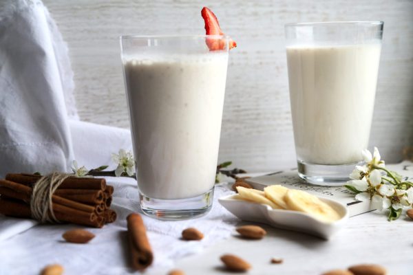 side view two glasses of milk with cinnamon and sliced ??banana and strawberrie