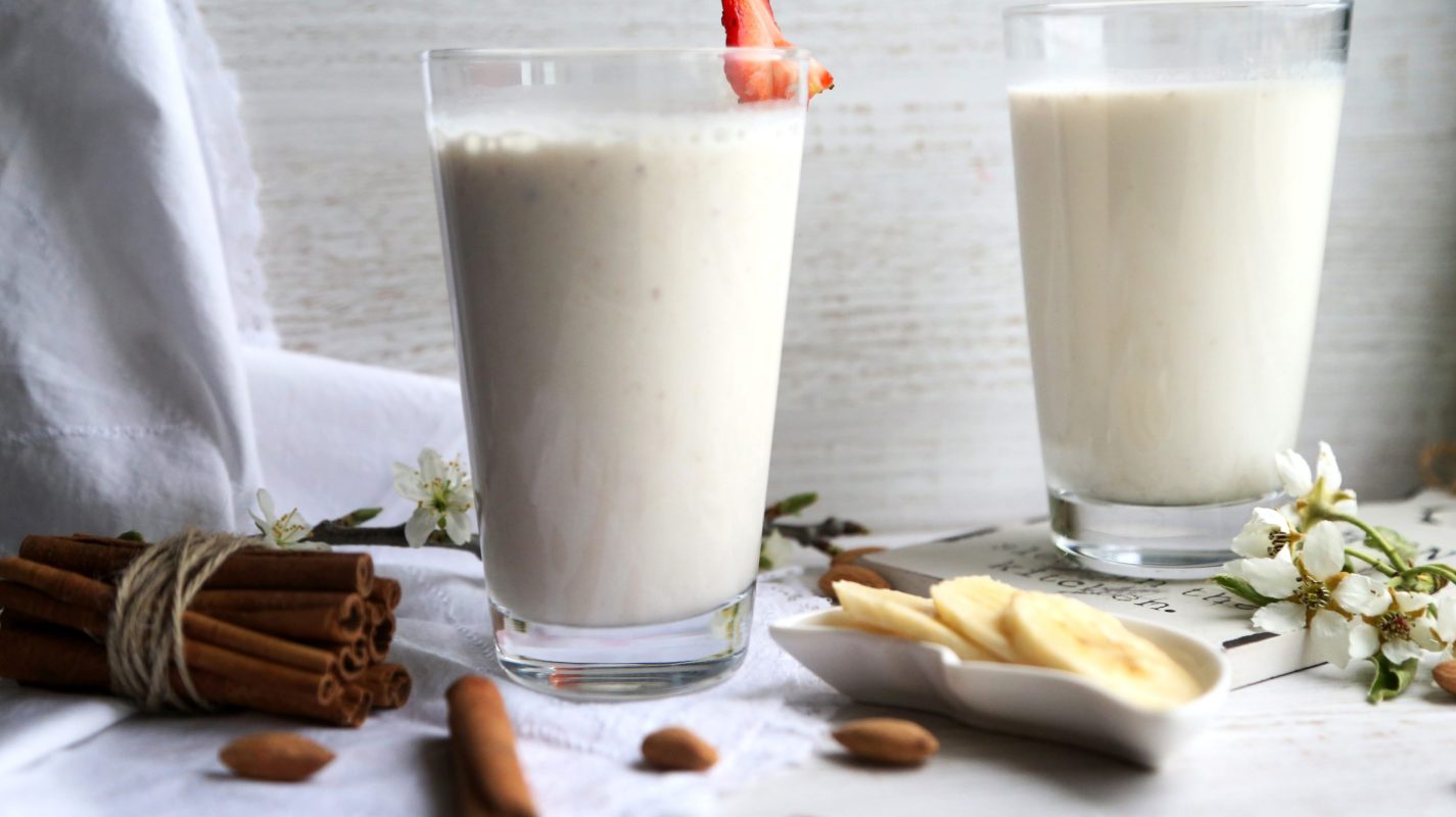 side view two glasses of milk with cinnamon and sliced ??banana and strawberrie