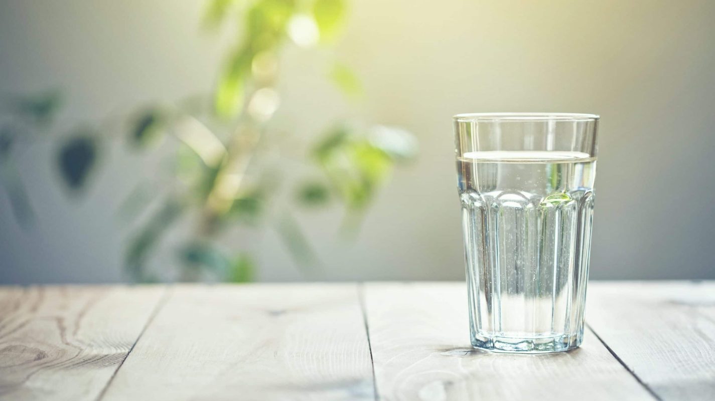 Glass of pure water on sunlight background with natural plant