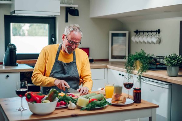 Elderly man preparing dinner for his family while cutting vegetables in the kitchen and cooking food meal at home. Portrait of a senior man in a modern kitchen. Copy space.